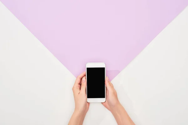 Cropped view of woman holding smartphone on violet and white background — Stock Photo