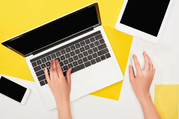 Cropped view of woman using laptop near gadgets on yellow and white background — Stock Photo