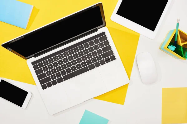 Вид зверху на ноутбук, цифровий планшет, смартфон з порожнім екраном та комп'ютерною мишкою на жовтому та білому тлі — стокове фото