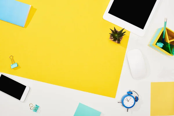 Top view of digital tablet, smartphone with blank screen and office supplies on yellow and white background — Stock Photo