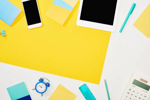 Вид сверху цифрового планшета, смартфона с чистым экраном и офисными принадлежностями на желтом и белом фоне с копировальным пространством — стоковое фото