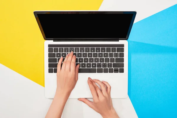 Vista recortada de la mujer usando el ordenador portátil con pantalla en blanco sobre fondo amarillo, azul y blanco - foto de stock