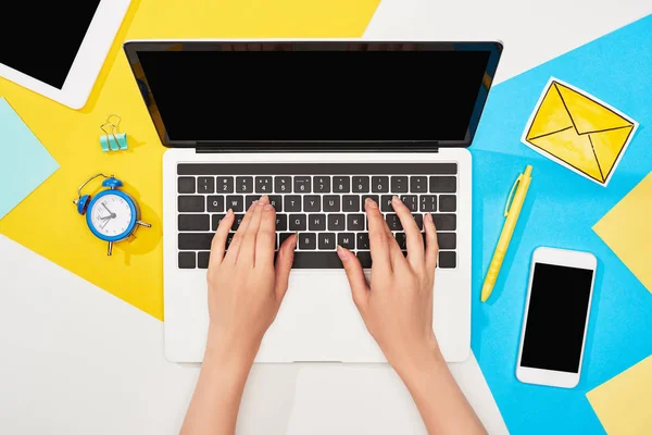 Cropped view of woman using laptop near office supplies and mail icon on yellow, blue and white background — Stock Photo