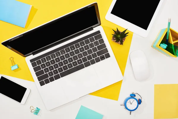 Vue du haut de l'ordinateur portable, smartphone, tablette numérique avec écran vierge et souris d'ordinateur avec fournitures de bureau sur fond jaune et blanc — Photo de stock