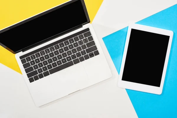 Top view of laptop, digital tablet with blank screen on yellow, blue and white background — Stock Photo