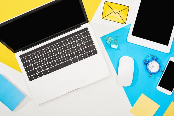 Vue de dessus des appareils numériques avec fournitures de bureau et icône du courrier sur fond jaune, bleu et blanc — Photo de stock