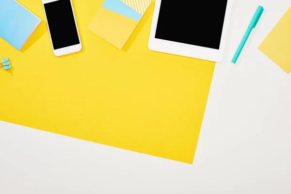 Top view of smartphone, digital tablet with blank screen with office supplies on yellow and white background — Stock Photo