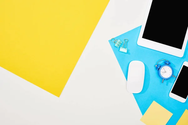 Top view of smartphone, digital tablet with blank screen and computer mouse with office supplies on yellow, blue and white background — Stock Photo