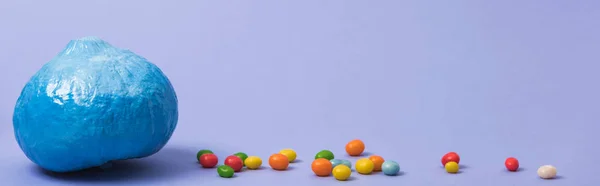 Panoramic shot of painted blue pumpkin with candies on violet background — Stock Photo