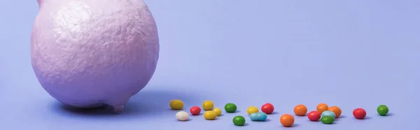 Panoramic shot of painted violet pumpkin with sweets on violet background — Stock Photo