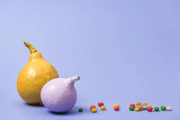 Painted pumpkins with candies on violet background — Stock Photo