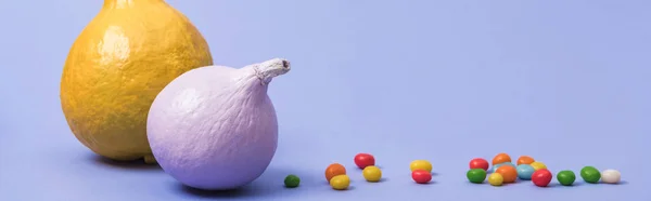 Panoramic shot of painted pumpkins with candies on violet background — Stock Photo