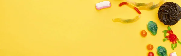 Panoramic shot of colorful gummy sweets and cupcake on yellow background, Halloween treat — Stock Photo