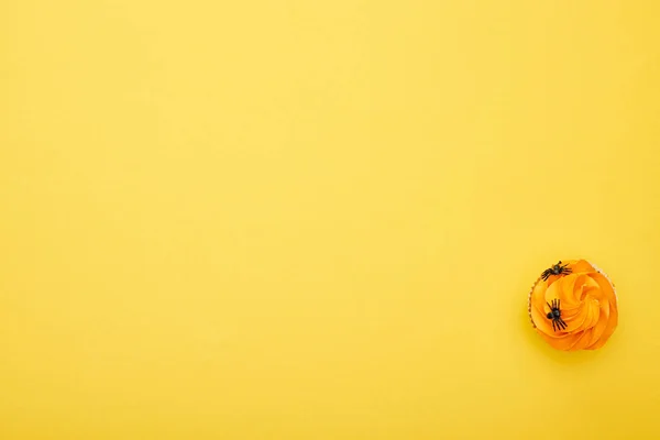 Vista superior de cupcake naranja con arañas sobre fondo amarillo, regalo de Halloween - foto de stock