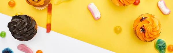 Plano panorámico de coloridos dulces gomosos y cupcakes sobre fondo amarillo y blanco, regalo de Halloween - foto de stock