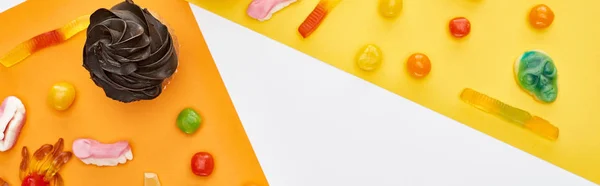 Plano panorámico de dulces gomosos y cupcakes sobre fondo amarillo y blanco, regalo de Halloween - foto de stock