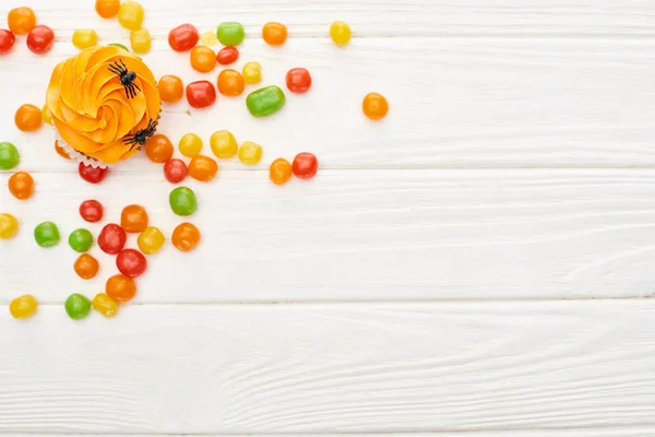 Vista superior de bonbons coloridos perto de cupcake com aranhas na mesa de madeira branca, deleite de Halloween — Stock Photo