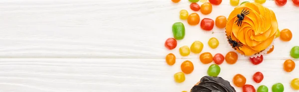 Plano panorámico de coloridos bombones y cupcakes en la mesa de madera blanca, regalo de Halloween - foto de stock