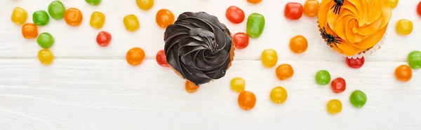 Top view of colorful bonbons and cupcakes on white wooden table, Halloween treat — Stock Photo