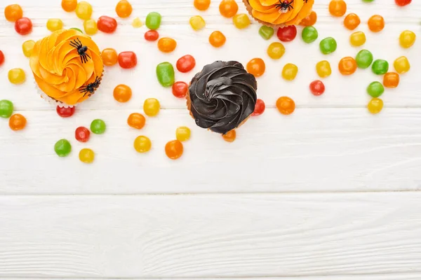 Top view of colorful bonbons and cupcakes on white wooden table, Halloween treat — Stock Photo