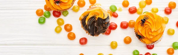 Top view of colorful bonbons and cupcakes on white wooden table, Halloween treat — Stock Photo