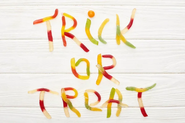 Top view of trick or treat lettering made of colorful gummy sweets on white wooden table with spiders, Halloween treat — Stock Photo