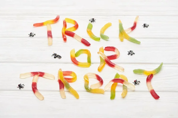 Trick- oder Leckerli-Schriftzug aus bunten Gummibonbons auf weißem Holztisch mit Spinnen, Halloween-Leckerbissen — Stockfoto