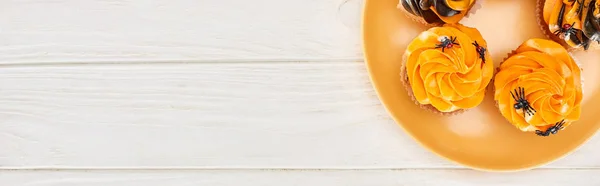 Вид зверху смачні кекси з павуками на помаранчевій тарілці на білому дерев'яному столі, Хеллоуїн — стокове фото