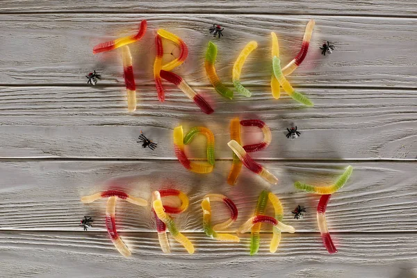 Vista superior de truco o tratar letras hechas de dulces de goma de colores en la mesa de madera blanca con arañas, regalo de Halloween - foto de stock