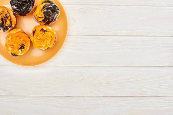 Top view of delicious cupcakes with spiders on orange plate on white wooden table, Halloween treat — Stock Photo