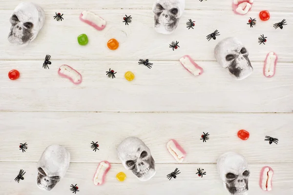 Vista superior de bombones, dientes de goma, calaveras y arañas en la mesa de madera blanca, regalo de Halloween - foto de stock