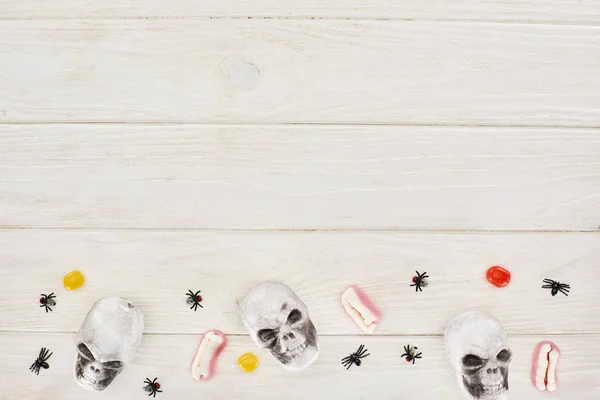 Vista superior de los bombones, dientes de goma, calaveras y arañas en la mesa de madera blanca con espacio para copiar, regalo de Halloween - foto de stock