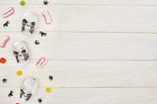 Draufsicht auf Bonbons, Gummizähne, Schädel und Spinnen auf weißem Tisch, Halloween-Leckerbissen — Stockfoto