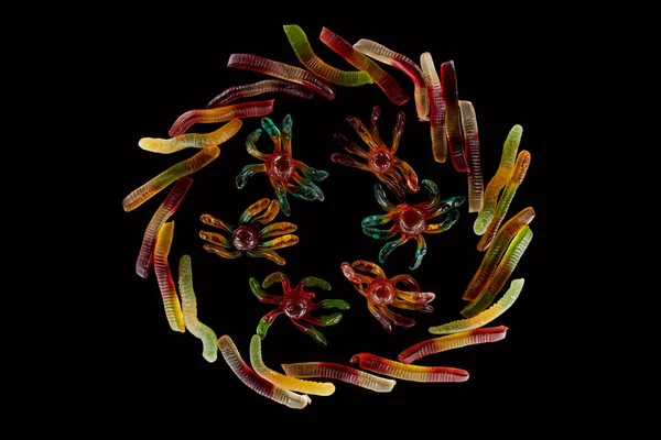 Top view of colorful gummy spiders in circle of worms isolated on black, Halloween treat — Stock Photo