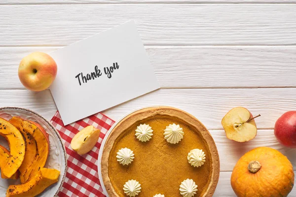 Vista dall'alto di torta di zucca con biglietto di ringraziamento su tavolo bianco di legno con mele — Foto stock