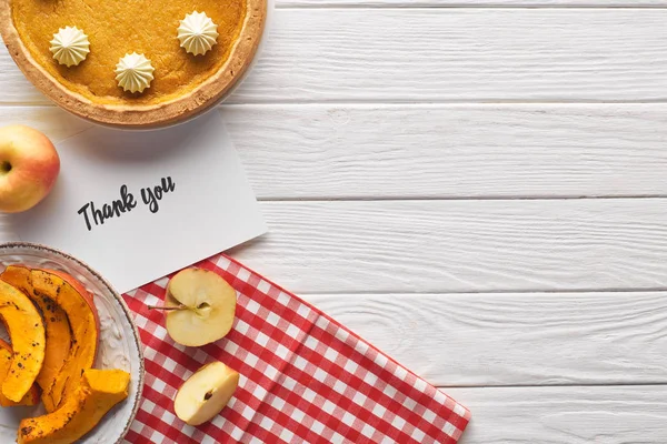 Vista dall'alto di torta di zucca con biglietto di ringraziamento su tavolo bianco di legno con mele — Foto stock