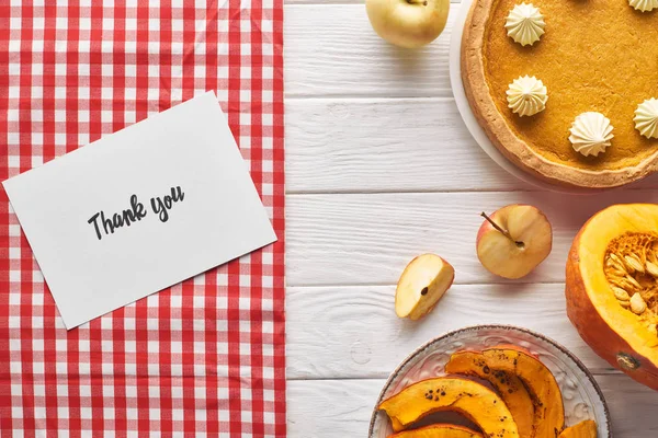 Vista dall'alto di torta di zucca con biglietto di ringraziamento su tavolo bianco di legno con mele — Foto stock