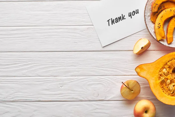 Vista superior de la tarjeta de agradecimiento en la mesa blanca de madera con manzanas y calabaza - foto de stock