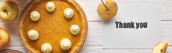 Vista dall'alto di deliziosa torta di zucca con biglietto di ringraziamento su tavolo bianco in legno con mele, colpo panoramico — Foto stock