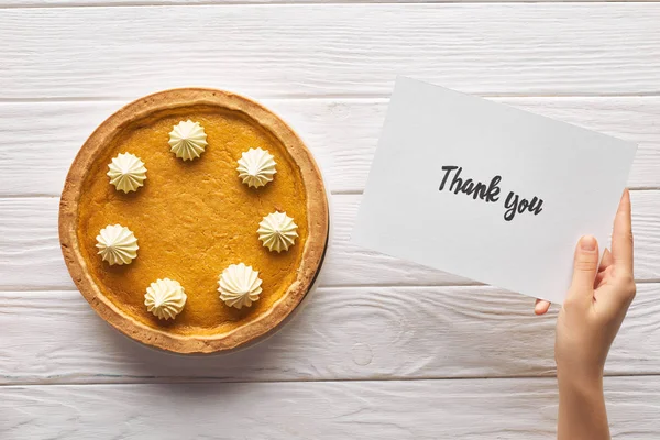 Vista ritagliata della donna in possesso di carta di ringraziamento vicino torta di zucca su tavolo in legno bianco — Foto stock