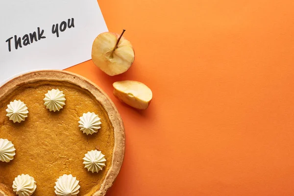 Vista dall'alto della torta di zucca con biglietto di ringraziamento su sfondo arancione con mele — Foto stock