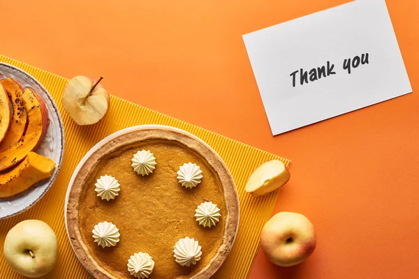 Vista dall'alto della torta di zucca con biglietto di ringraziamento su sfondo arancione con mele — Foto stock