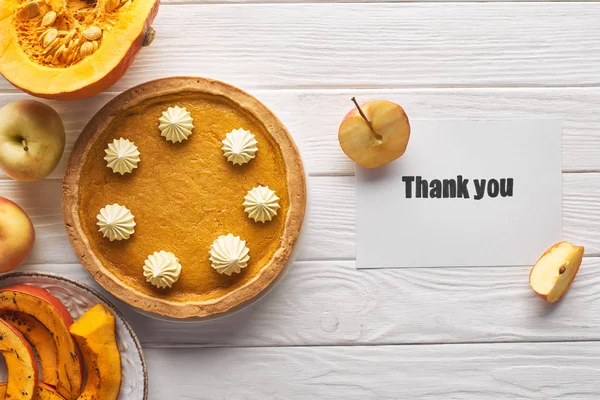 Vista superior de pastel de calabaza con tarjeta de agradecimiento en la mesa blanca de madera con manzanas - foto de stock