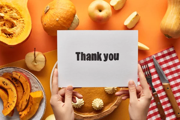 Cropped view of woman holding thank you card near pumpkin pie on orange background — Stock Photo