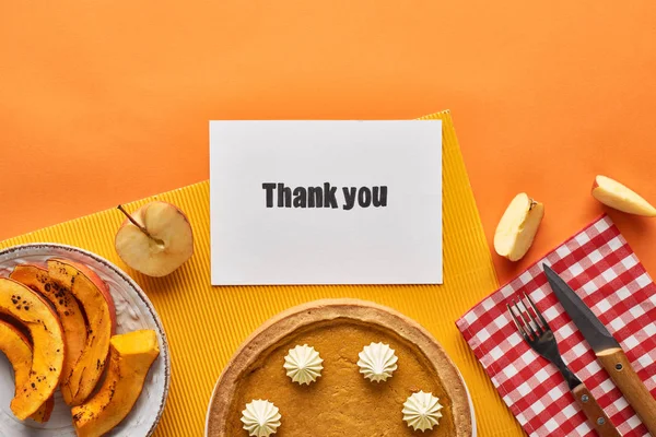 Vista superior de delicioso pastel de calabaza con tarjeta de agradecimiento sobre fondo naranja con manzanas - foto de stock