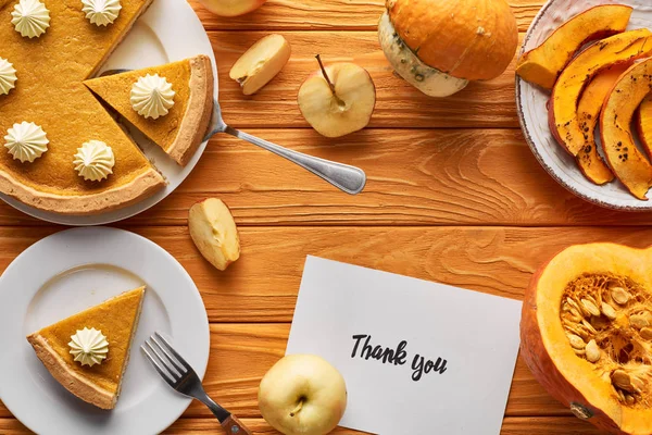 Vista superior de delicioso pastel de calabaza, manzanas y tarjeta de agradecimiento en la mesa naranja de madera - foto de stock