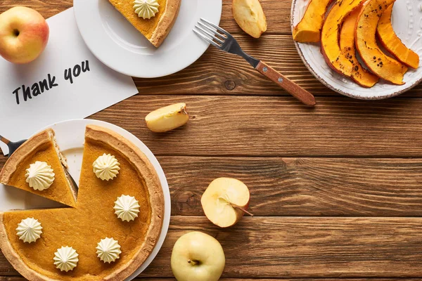 Vue de dessus de tarte à la citrouille savoureuse, pommes et carte de remerciement sur table rustique en bois — Photo de stock