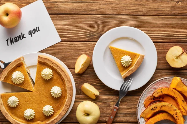 Vue de dessus de tarte à la citrouille savoureuse, pommes et carte de remerciement sur table rustique en bois — Photo de stock