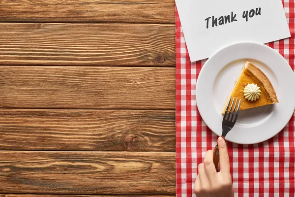 Cropped view of woman eating pumpkin pie on plaid napkin with thank you card on wooden table — Stock Photo