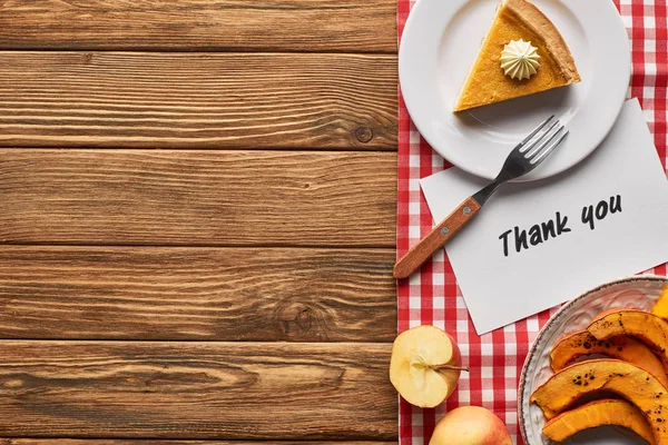 Vista superior del delicioso pastel de calabaza, manzanas y tarjeta de agradecimiento en la mesa rústica de madera con servilleta a cuadros - foto de stock